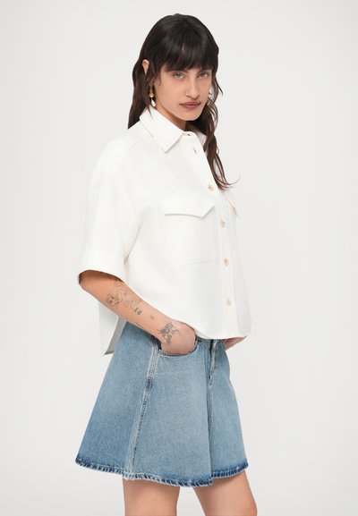 Λευκό πουκάμισο με κοντά μανίκια και γιακά, με κουμπώματα και δύο τσέπες στο στήθος, συνδυασμένο με φούστα A-line από τζιν σε ανοιχτό μπλε χρώμα.