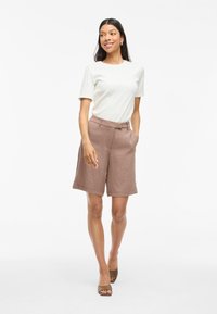 T-shirt grigio chiaro a maniche corte abbinato a pantaloni corti marroni fino al ginocchio. I pantaloni hanno una superficie liscia e tasche laterali.