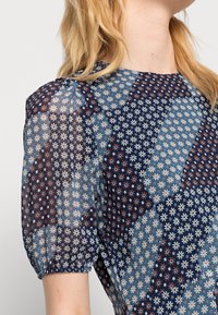 Floral print blouse with short puff sleeves, featuring a mix of blue, navy, and maroon patterns on sheer fabric.