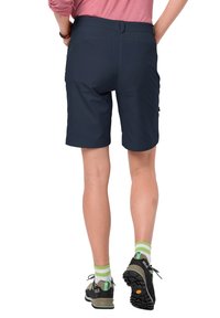 Námořnické modré kraťasy s hladkým povrchem, poutka na pásek v pase a boční kapsy; spárované s černými turistickými botami a ponožkami se zelenými pruhy.