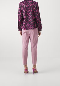 Mustapaita, jossa on vaaleanpunainen huulikuosi, yhdistettynä vaaleanpunaisiin räätälöityihin housuihin ja vaaleanpunaisiin korokepolkujen kenkiin. Näkymä on takaa.