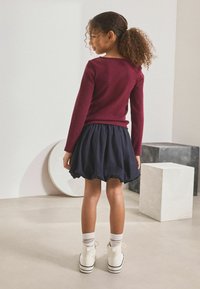 Bordeaux ribbel lange mouwen top gecombineerd met een marineblauwe puff rok. Witte hoge sneakers en kniehoge gestreepte sokken. Eenvoudig, modern ontwerp.