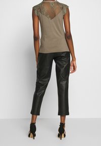 Olive green sleeveless top with lace overlay at shoulders, paired with black faux leather cropped pants and black high-heeled shoes.