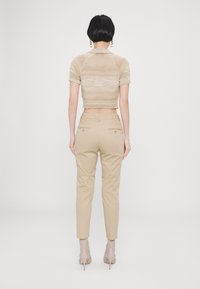 Béžové krátké polo tričko s krátkými rukávy a pletenou texturou. Béžové kalhoty na míru s zadními kapsami a zlatými knoflíky.