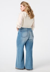Lichtbeige top met ruches, gecombineerd met hoge taille, wijde blauwe jeans. Zichtbare achterzakken en vervaagde denimtextuur.