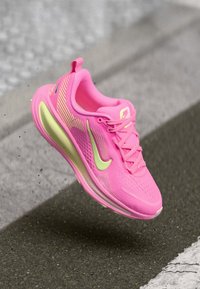 Rosa Sportlichkeitsschuh mit einem leichten Mesh-Obermaterial, strukturiertem Design und einer durchsichtigen gelben Sohle. Nike-Logo in kontrastierendem Grün.