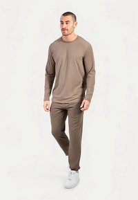 Lichtbruine blouse met lange mouwen gecombineerd met bijpassende broek, beide gemaakt van gladde stof. Draag ze met witte sneakers, simpel ontwerp met ronde hals.