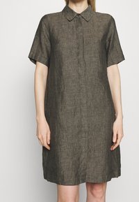 Lyhythihainen, ruskea pellavamekko, jossa on kaulus, nappikiinnitys ja rento malli. Mekossa on hienovarainen rakenne ja polvipituinen muotoilu.