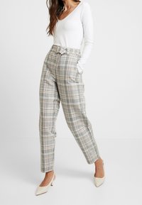 Karierte hoch taillierte Hose in Beige, Grau und sanftem Orange mit Seitentaschen und einem Gurtbund, kombiniert mit einem weißen Langarmoberteil.