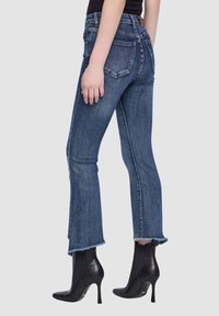 Jeans blu scuro alla caviglia con orlo svasato, leggera usura e due tasche posteriori. Indossati con stivaletti neri con tacco.