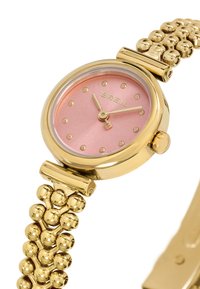 Guld-tone ur med rund kasse, pink urskive og punktmarker. Har et tekstureret guldarmbånd med sfæriske accenter på båndet.
