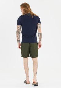 Navyblå bomullströja med korta ärmar, kombinerad med olivgröna shorts. Shortsarna är rullade vid fållen, och modellen har mörka slip-on sandaler.