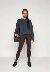 Mörkblå kort tröja, ribbade bruna leggings, svarta sneakers och en liten svart väska. Enkelt mönster, avslappnad atletisk stil.