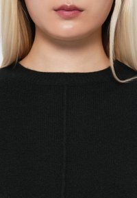 Maglione nero a maglia con scollo rotondo, texture morbida e dettagli di cucitura sottili al centro, che mette in mostra un design elegante e minimalista.