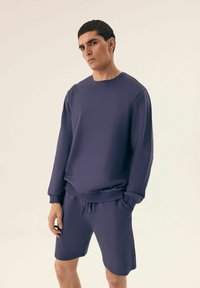 Fioletowy zestaw z bluzy i szortów wykonany z gładkiego, lekkiego materiału. Bluza ma okrągły dekolt, a szorty posiadają regulowany pas.