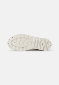 Suola di una scarpa, realizzata in materiale gommoso beige texturizzato. Il design include un motivo a zigzag e lugs circolari per maggiore aderenza.