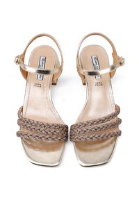 Sandali in pelle dorata con punta quadrata, tre cinturini intrecciati marroni e una piccola fibbia sulla cinghia alla caviglia. Fodera interna liscia.