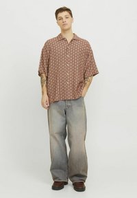 Camisa de manga corta con estampado en tonos marrones, combinada con jeans de corte holgado y lavado claro. Unos zapatos marrones completan el conjunto.