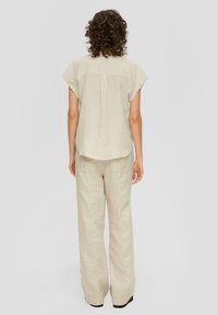 Beige linnen top met korte mouwen en een gebogen zoom, gecombineerd met beige linnen wijde broek met twee achterzakken. Eenvoudig en gestructureerd ontwerp.
