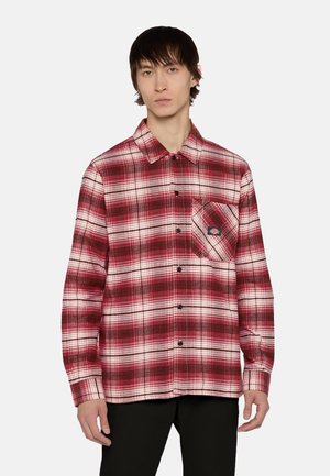 Camisa de franela a cuadros rojos y blancos con mangas largas, cierre de botones y bolsillo en el pecho con una etiqueta de logo.