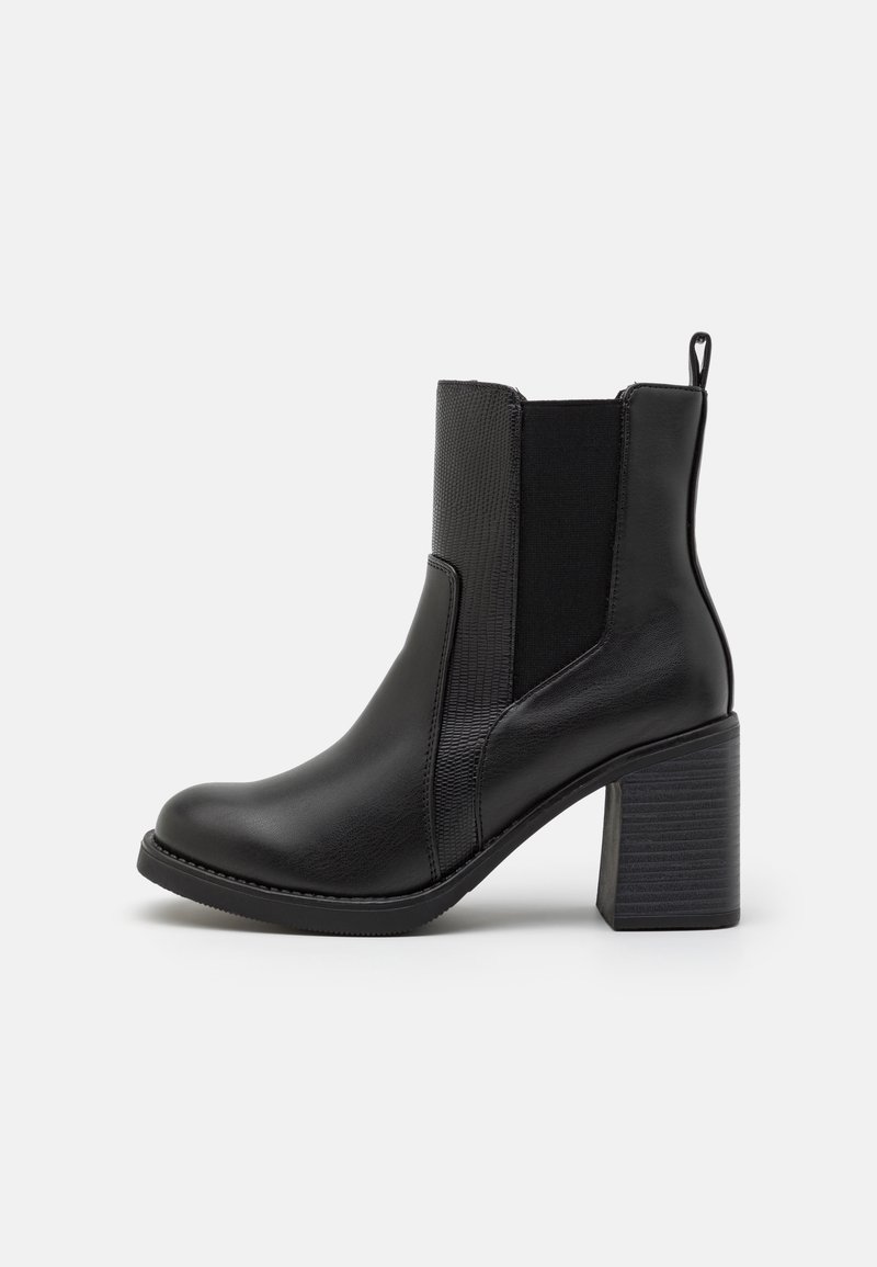 Musta nahkasaapas nilkkapituisena, jossa on tukevat korot, joustavat sivupaneelit ja vetoketju, esiteltynä ulkopuolelta valkoista taustaa vasten.