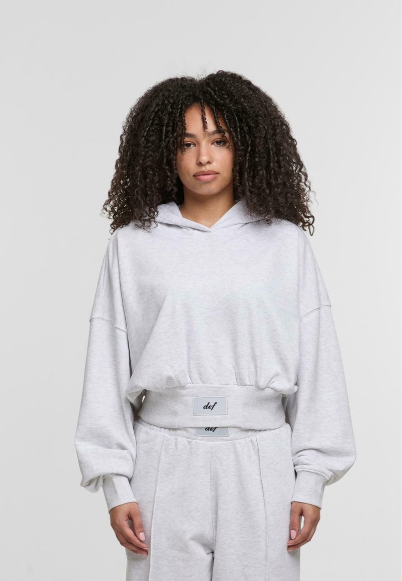 Hoodie grigio corto con vestibilità morbida, dotato di cappuccio con cordino, maniche oversize e un bordo a costine in vita con etichette logo.