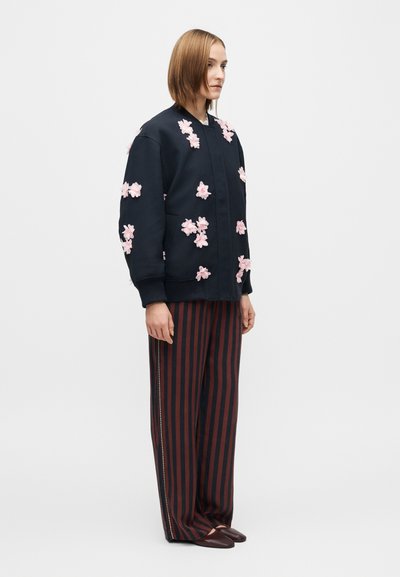 Jachetă bomber neagră cu broderie florală roz, cu manșete striate, asortată cu pantaloni cu dungi roșii și bleumarin, cu croială lejeră și textură netedă.