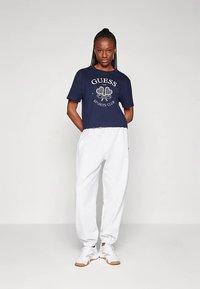 Námořnicky modré zkrácené tričko s bílým logem, doplněné volnými bílými tepláky a bílými teniskami s hnědými detaily. Jednoduchý design, pohodlný střih.