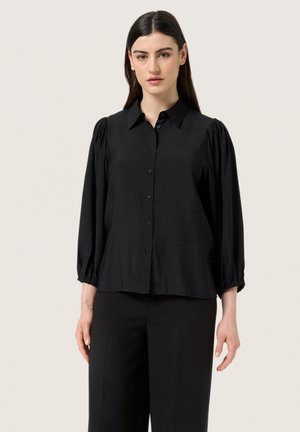 Blusa nera in tessuto morbido, con chiusura a bottoni sul davanti, colletto e maniche lunghe a sbuffo con polsini elasticizzati.