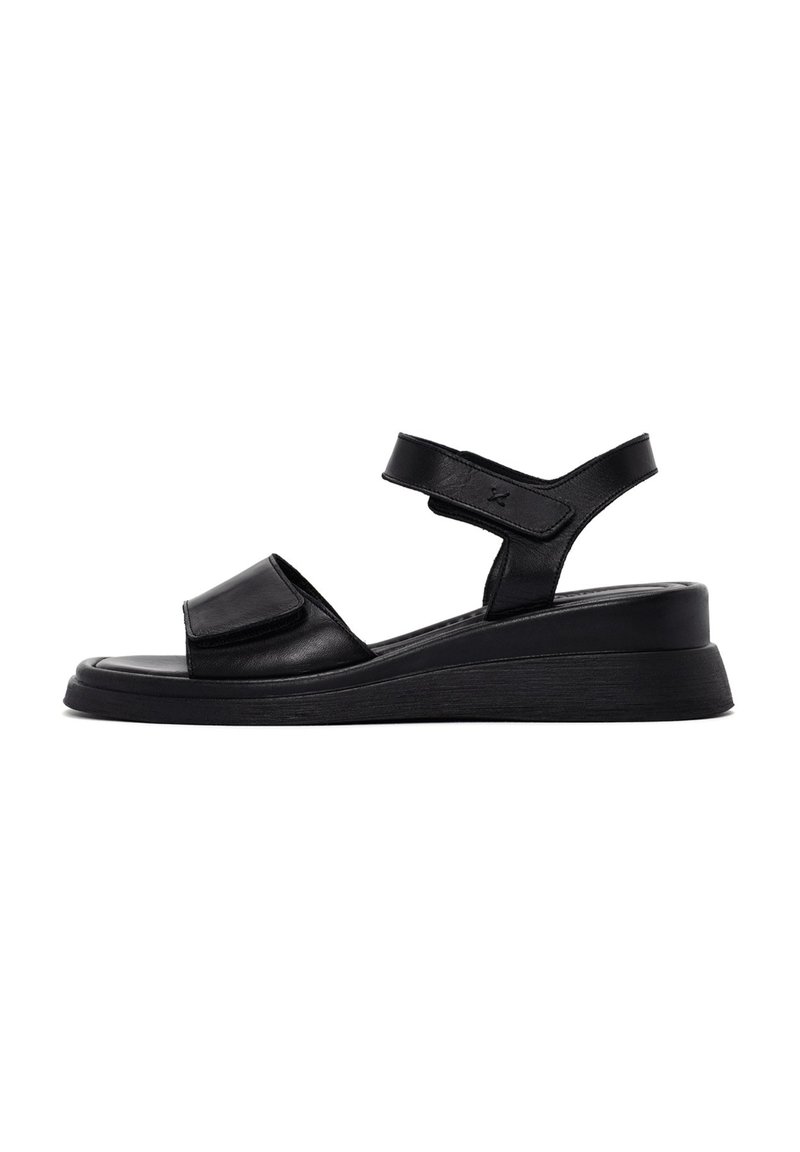 Sandali in pelle nera con una larga fascia frontale, cinturino alla caviglia regolabile e una suola a zeppa bassa per ulteriore supporto e comfort.