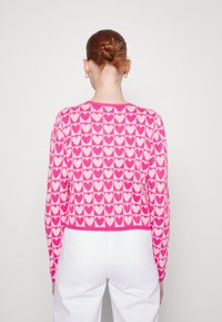 Różowy sweter dziany z wzorem serca w jaśniejszym odcieniu różu, krótki fason z długimi rękawami, okrągłym dekoltem i prążkowanym wykończeniem.