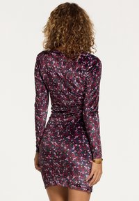 Fioletowa aksamitna sukienka w kwiaty z długimi rękawami, dopasowaną sylwetką i długością do kolan. Posiada wielokolorowy wzór kwiatowy na całej powierzchni.