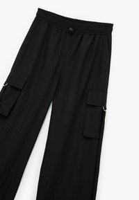 Pantalones cargo negros hechos de una tela ligera. Presentan una cinturilla elástica, dos bolsillos laterales y dos bolsillos cargo con cierres de botón.