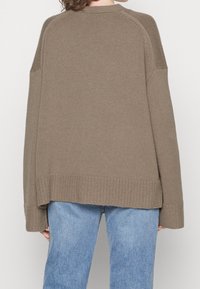 Brauner Strickpullover mit überschnittenen Schultern, geripptem Saum und Texturmuster. Kombiniert mit blauen Jeans in lässiger Passform.