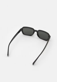 Ochelari de soare dreptunghiulari negri, cu o ramă din plastic lucios și lentile gri închis. Brațe drepte care se subțiază la capete. Design minimalist.