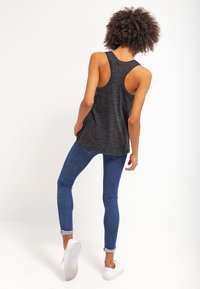 Grå ärmlös linne med rundad bak, kombinerad med mörkblå skinny jeans och vita sneakers, visar en avslappnad outfit bakifrån.