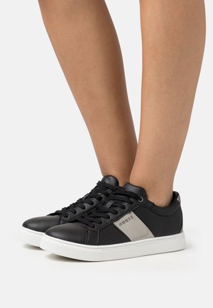 Baskets en cuir noir avec une semelle blanche et des lacets plats. Présentent un accent gris sur le côté avec un logo. Texture lisse avec un bout arrondi.