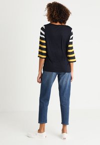 Marine t-shirt met zwart, wit en gele gestreepte driekwartmouwen, gecombineerd met cropped blauwe jeans en witte sneakers.