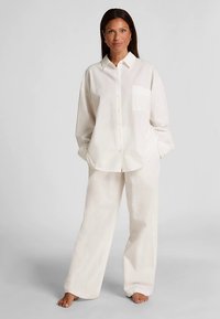 Witte, gestructureerde blouse met knopen en een borstzak, gecombineerd met bijpassende wijde broekspijpen, ontworpen voor een ontspannen pasvorm.