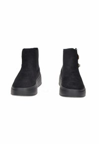 Un paio di stivali alla caviglia in suede neri con suole in gomma spessa, vista frontale, design semplice con pannelli elasticizzati laterali e fibbie decorative su un lato.