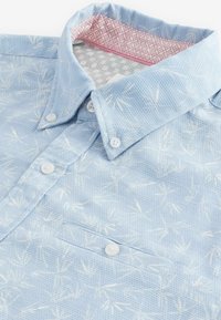 Lys blå button-up skjorte med en tekstureret stof, hvidt bladmuster og en lyserød mønstret indvendig krave. Har en brystlomme og hvide knapper.