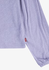 Ανοιχτό μωβ πουκάμισο μακρυμάνικο φτιαγμένο από μαλακό ύφασμα, με ελαστικούς καρπούς και μια μικρή κόκκινη ετικέτα στο πλάι με το λογότυπο της μάρ�κας.