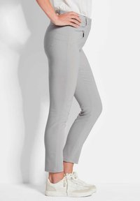 Lichtgrijze slim-fit broek met een gladde textuur, voorzien van een ritszak aan de voorkant en zijnaad, gecombineerd met witte sneakers.