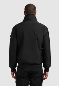 Jachetă izolată neagră cu guler înalt, manșete elastice și talie ribbed. Include branding subtil pe spate.