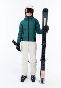 Slidinėjimo apranga apima šviesiai mėlyną pūkinę striukę, kreminės spalvos slidinėjimo kelnes ir juodus batus. Aksesuarai - šalmas, akinių lęšiai ir slidžių lazdos su slidėmis.