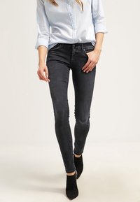 Jeans slim negros con una textura suave, talle medio y un ligero desgastado. Combinados con una camisa azul clara y botas negras de tobillo.