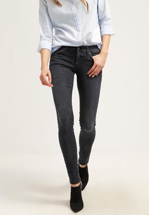 Jeans skinny neri con una texture liscia, vita media e una leggera sfumatura. Abbinati a una camicia azzurro chiaro e stivali neri alla caviglia.