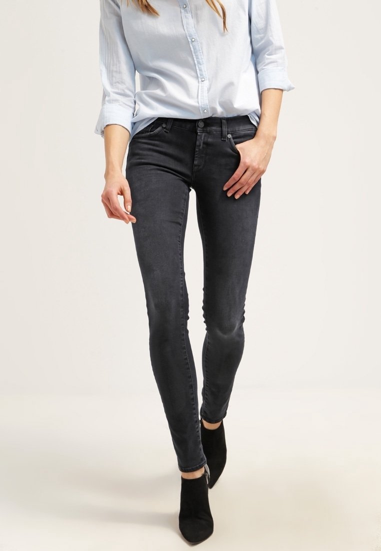 Jeans slim negros con una textura suave, talle medio y un ligero desgastado. Combinados con una camisa azul clara y botas negras de tobillo.
