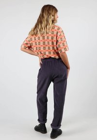 Chemise à manches courtes avec des motifs de carrés orange, verts et blancs. Associée à un pantalon en velours côtelé bleu marine et des chaussures noires.