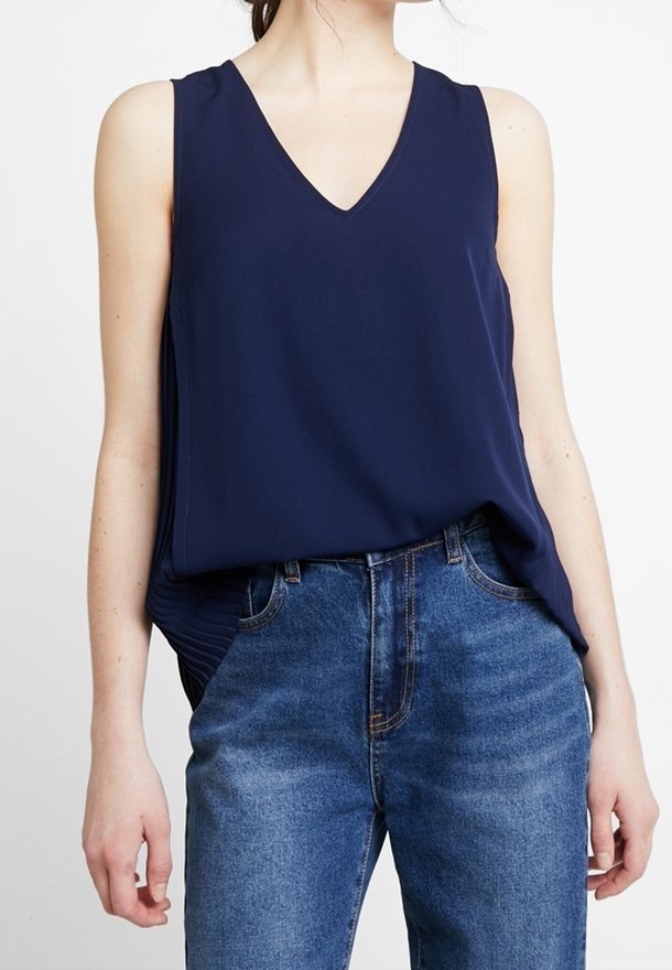 Haut sans manches bleu marine avec un col en V, tissu doux, coupe décontractée et détails sur les côtés ; assorti à un jean en denim bleu avec une coupe classique.